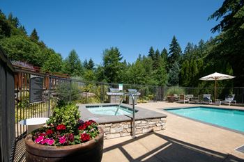 A pool surrounded by a fence and trees with a hot tub in the middle. at Lakemont Orchard Apartments, Issaquah 